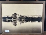 an old photo of a building on a lake with mountains in the background