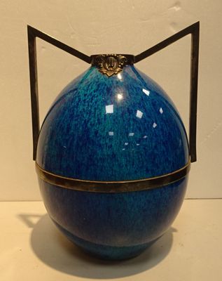 un vase bleu posé sur une table, muni d'une anse noire