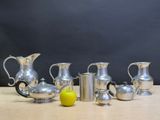 five silver pitchers and a lemon on a table