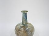un petit vase en verre avec un couvercle vert posé sur une surface blanche
