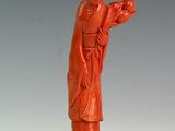 une statue orange représentant un homme tenant un oiseau, posée sur un socle en bois