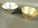 pair of silver bowls on a table with a gray background