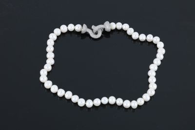 un collier de perles blanches muni d'un fermoir en argent, posé sur un fond noir
