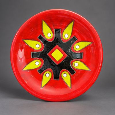 une assiette rouge ornée de motifs jaunes et noirs