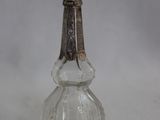 un flacon de parfum ancien en verre, muni d'une poignée en métal, posé sur une surface blanche