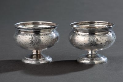 une paire de tasses argentées posées sur une surface grise avec un fond noir