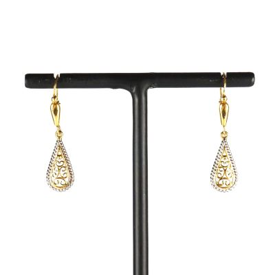 une paire de boucles d'oreilles en or et diamants posée sur un socle noir