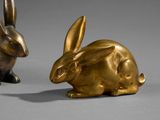 pair of bronze rabbits sitting next to each other on a gray surface