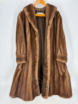 un manteau de fourrure marron suspendu à un cintre sur fond blanc