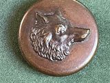 un badge en métal sur lequel est représenté un loup
