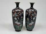 two black vases with flowers on them on a white surface