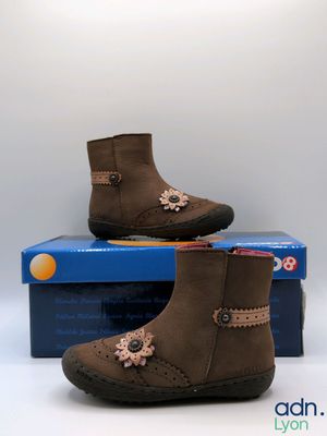 une paire de bottes marron pour enfants posée sur une boîte bleue