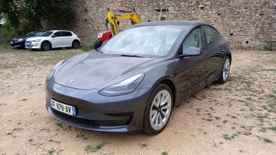 La Tesla Model 3 est garée devant un bâtiment en pierre.