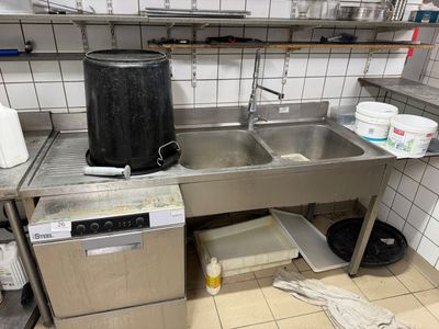 a kitchen with a sink, stove, and trash can in it