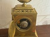 a gold clock sitting on a wooden table with a clock on top of it