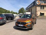 La voiture orange est garée devant un immeuble sur lequel est accrochée une pancarte.
