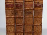 four old books are lined up in a row on a white surface
