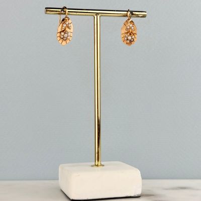 a pair of gold earrings on a marble stand