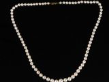 un collier de perles blanches avec un fermoir en or sur fond noir