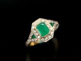 an emerald and diamond ring on a black surface