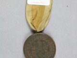 une vieille médaille en bronze entourée d'un ruban, posée sur une surface blanche