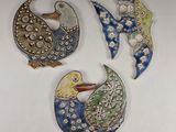 three decorative birds are sitting next to each other on a white surface