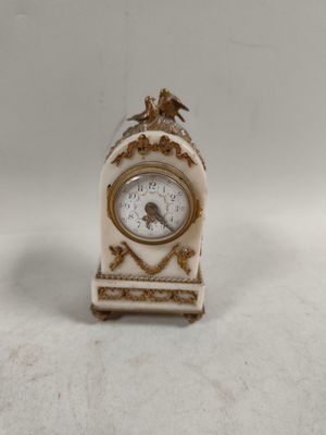 une petite horloge blanche surmontée d'un oiseau