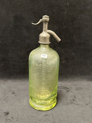 une vieille bouteille en verre vert munie d'une poignée en métal, sur fond noir