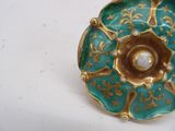 a green and gold plate with a pearl in it