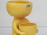 un vase jaune posé sur une table, dans lequel se trouve une tasse