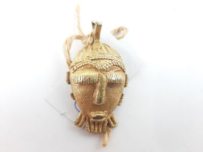 a close up of a gold pendant with a face on it