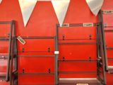 Plusieurs échelles sont alignées contre un mur rouge dans une pièce.