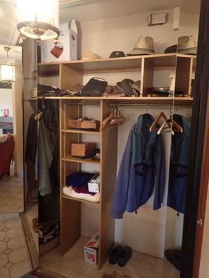 un placard avec des vêtements suspendus aux étagères et une chaise à l'arrière-plan