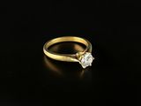 a gold engagement ring with a single diamond on a black surface