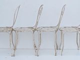 three white metal chairs sitting next to each other on a white surface