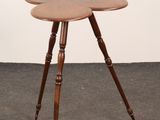 une petite table en bois à trois pieds, dont le plateau a la forme d'une fleur