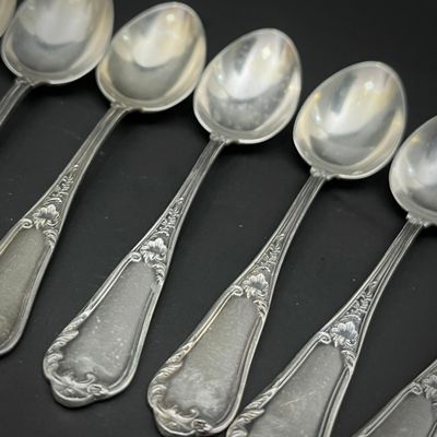 six cuillères en argent sont alignées sur une surface noire