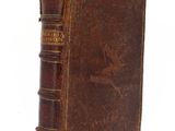 un vieux livre brun posé sur une table à côté d'un mur blanc