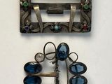 two pieces of silver and blue glass brooches on a white surface