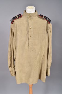 une chemise beige avec des bordures noires et rouges, posée sur un présentoir pour mannequin