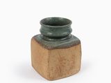 petit vase en céramique verte avec un socle en bois, posé sur une surface blanche