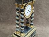a black and gold clock on a stand on a brown background
