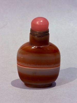 a small glass bottle with a pink top on a white surface