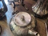 a wooden table topped with silver tea pots and silver spoons