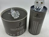 une figurine de chouette en argent dans une boîte en fer-blanc, à côté d'un coffret en argent