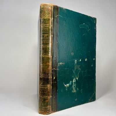 an old book with a green cover sitting on a white surface