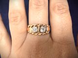 a woman ' s hand holding a gold ring with three diamonds on it