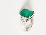 an emerald and diamond ring with baguets on a white surface