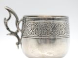 an antique silver cup on a white surface with a spoon in the middle