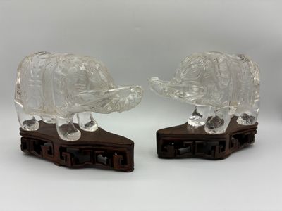 une paire d'éléphants en verre transparent posés sur des socles en bois, sur fond blanc